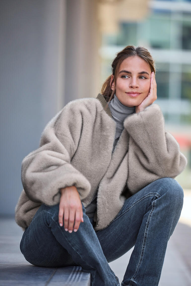 Beige Bomberjacke aus Kunstfell, lässig über die Schultern gelegt