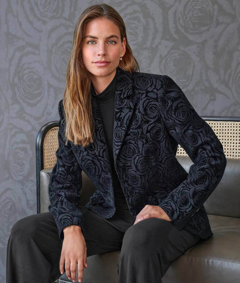 Frau in floral-gesticktem Blazer sieht direkt in die Kamera.