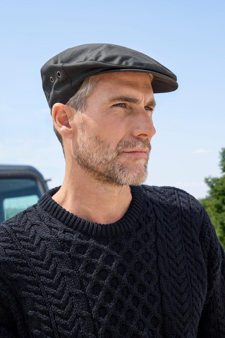 Waxed Cotton Schiebermütze Mann trägt eine schwarze gewachste Baumwoll-Schiebermütze im Freien.