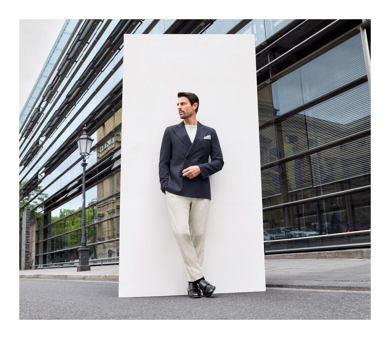 Mann in blauem Blazer und beigen Hosen posiert auf dem Gehweg.