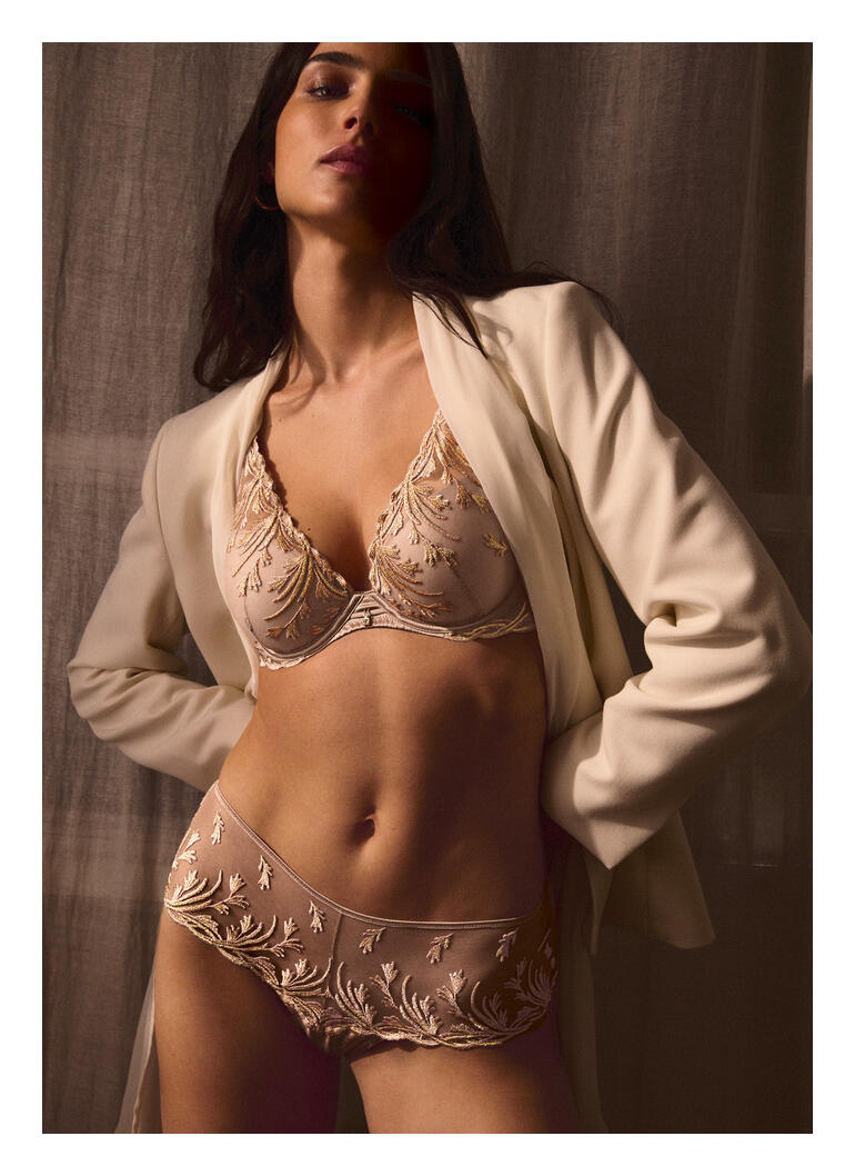 Damen-BH mit zarten Verzierungen in Sandfarbe vor neutralem Hintergrund.