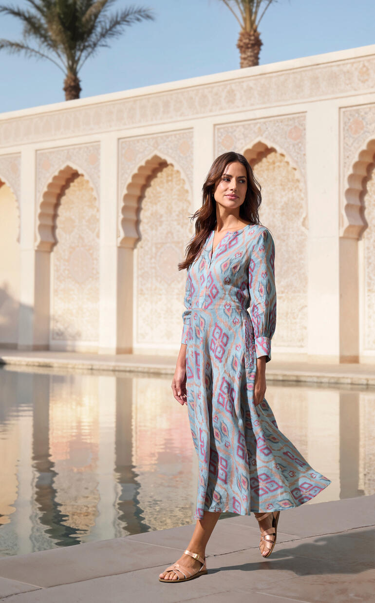 Frau in farbigem Ikat-Kleid neben einem Pool im Freien.