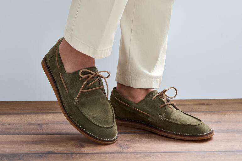 Astorflex Bootsschuh in olivgrün, getragen auf einem hellen Holzboden.