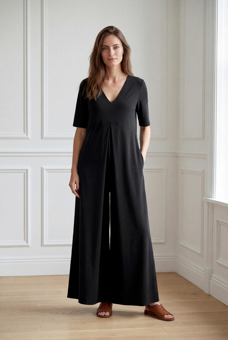 Frau trägt einen schwarzen Jersey-Jumpsuit und steht lächelnd in einem hellen Raum.