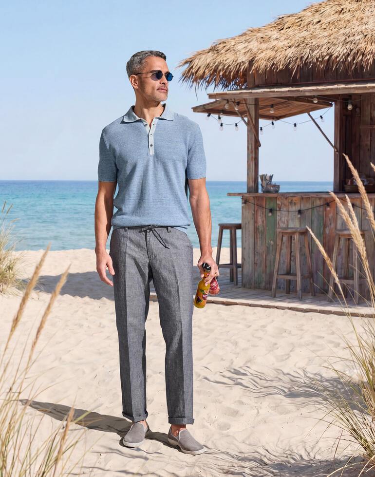 Mann in hellblauem Polohemd steht am Strand