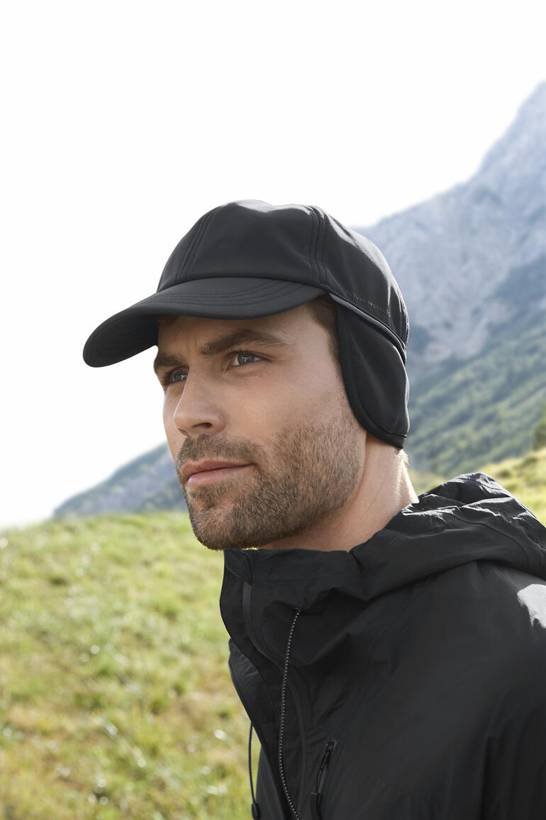 Mann mit schwarzer Softshell-Kappe und Jacke im Freien.