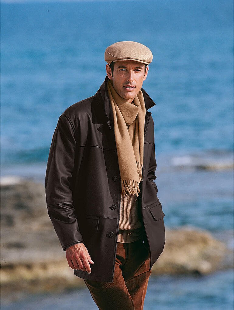 Mann trägt eine Kamelhaar-Mütze und Schal mit Blick auf das Meer.