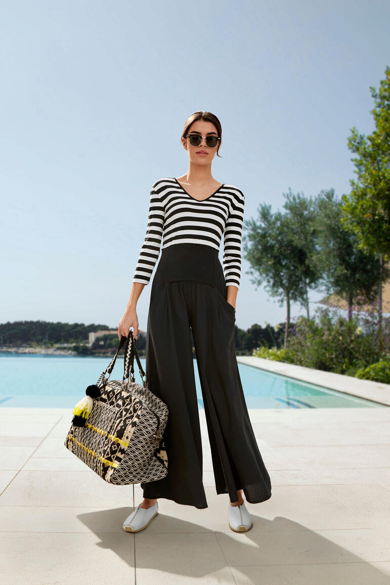 Smitten Weekender Manju Frau trägt einen gestreiften Ibiza-Hosenrock und hält eine Tasche.