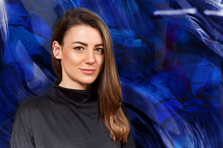 Michèle Caspers Porträt von Michèle Caspers vor einem blauen, abstrakten Hintergrund.