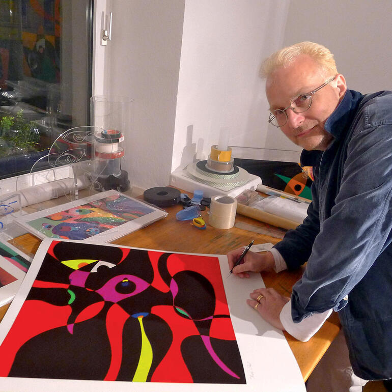 Der Künstler bei der Signatur der Edition. Der Künstler R. O. Schabbach bei der Arbeit an seinem Kunstwerk am Tisch.