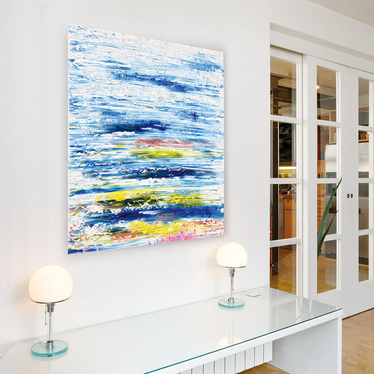 Aufgrund seiner farbigen Vielschichtigkeit entwickelt das Werk eine Eigendynamik, die jeden Raum bereichert. Abstraktes Kunstwerk hängt an einer weißen Wand über einem modernen Tisch