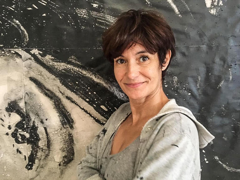 Frau mit Kurzhaarschnitt lächelt vor einem abstrakten Kunstwerk.