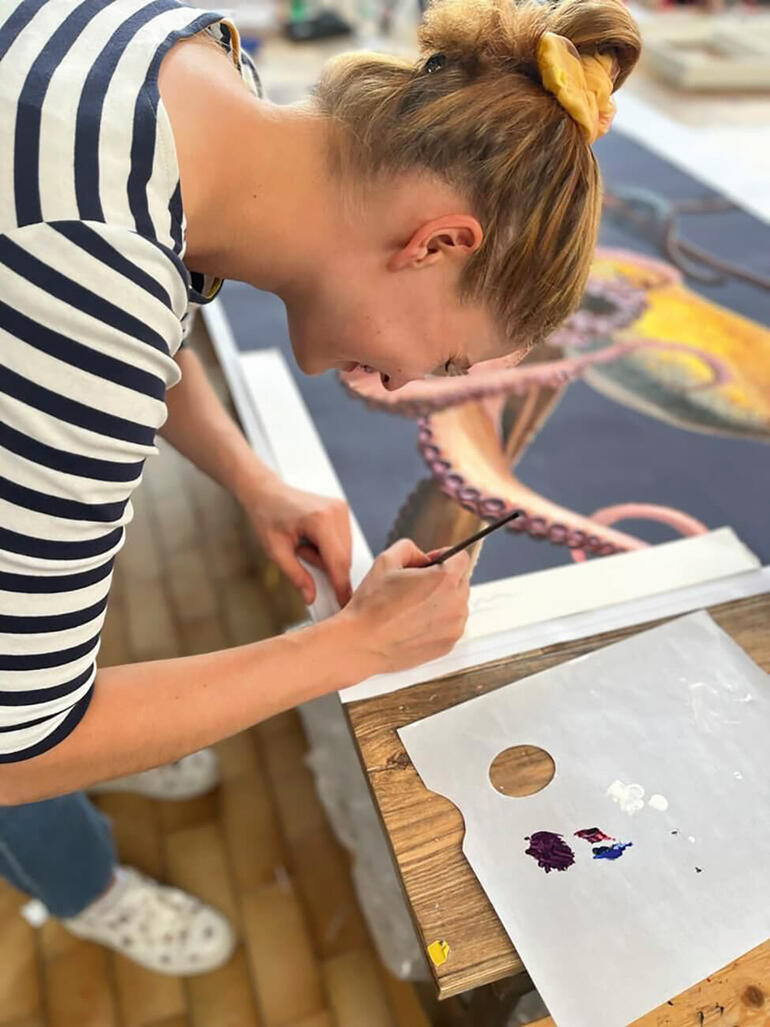 Eine Künstlerin malt an einem großen Bild eines Oktopusses in einem Atelier.