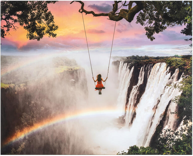 Mädchen schwingt auf einer Schaukel über den Victoria Falls mit farbenfrohem Himmel.
