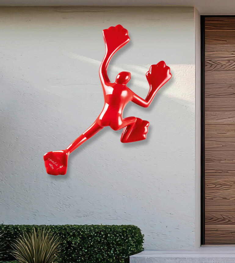 Rotere Skulptur an einer hellen Wand im Außenbereich.