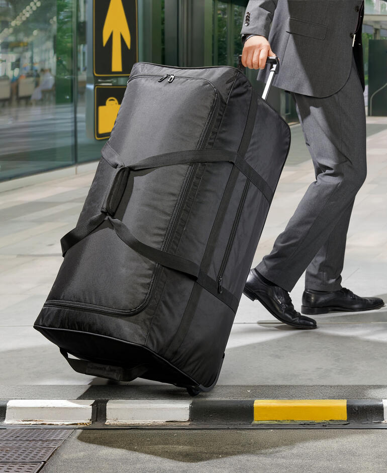 Schwarze Ultraleicht-XXL-Reisetasche wird von einem Mann im Anzug geschoben.