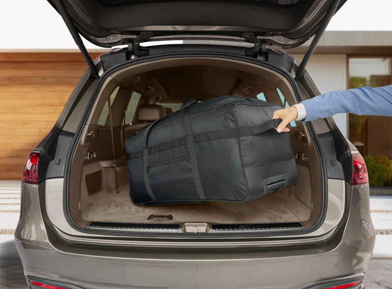 Schwarze Reisetasche wird im Kofferraum eines Autos verstaut.