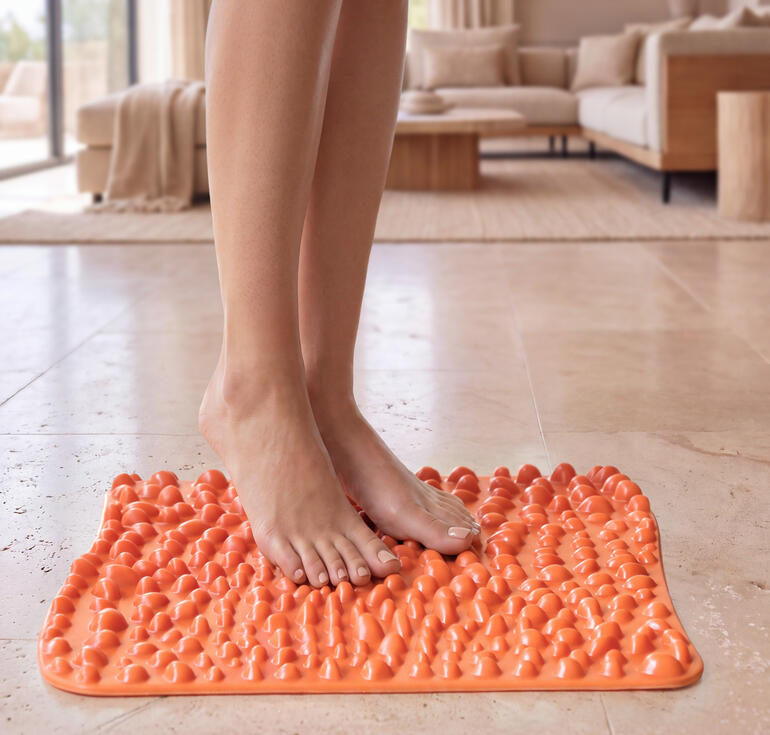 goFit-Fußreflexzonenmatte in leuchtendem Orange, auf einem hellen Fußboden mit Füßen darauf.