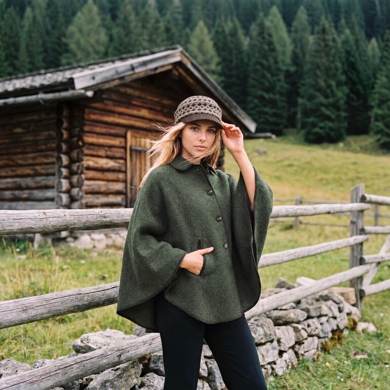 Frau mit grünem Cape und Mütze in einer ländlichen Landschaft