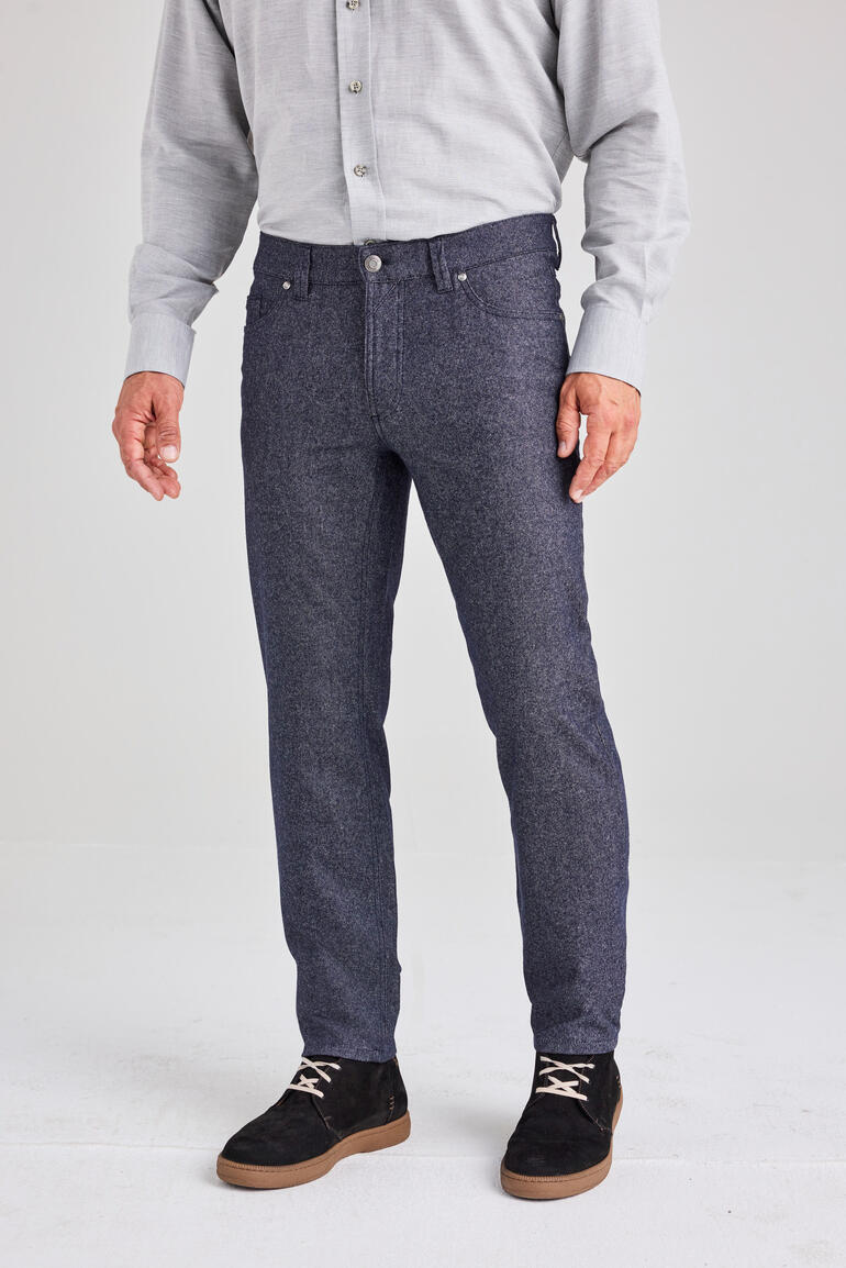 Mann mit grauem Hemd und Woll-Jeans steht auf einem hellen Hintergrund