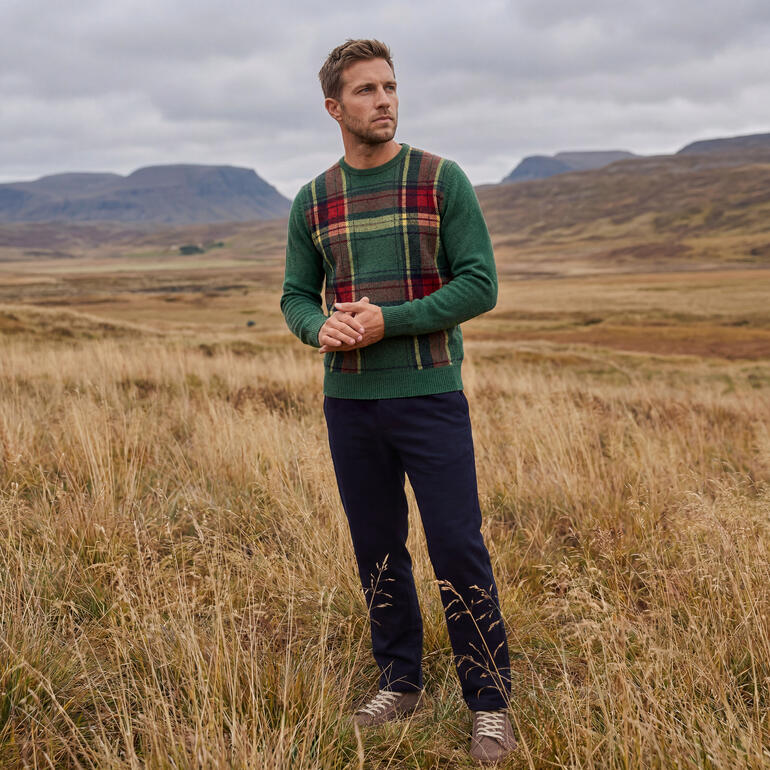 Mann in grünem Tartan-Pullover steht in einer herbstlichen Landschaft.