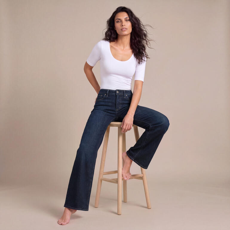 Frau in weißen T-Shirt und bequemen Jeans sitzt auf einem Hocker