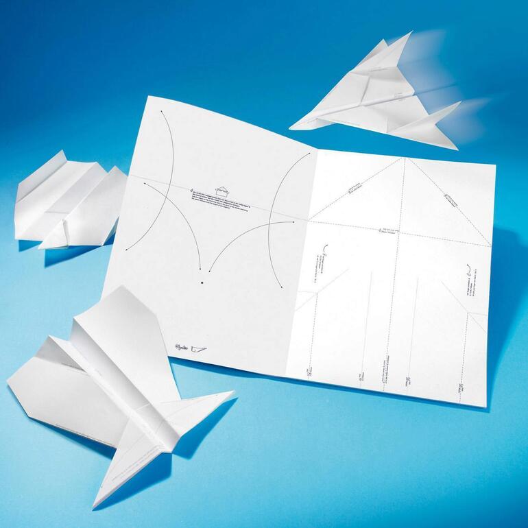 Papierflugzeuge und eine Anleitung zum Falten von Flugzeugen auf blauem Hintergrund.