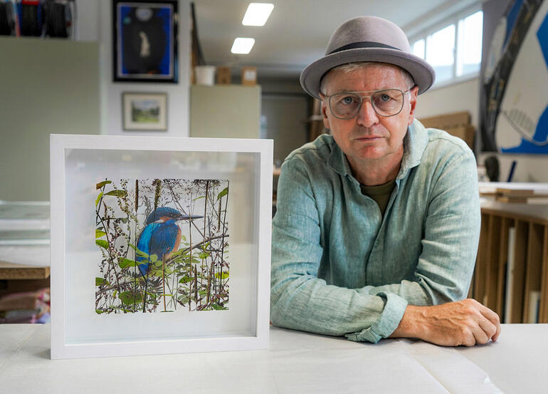 Andreas Lutherer Mann mit Hut sitzt neben einem Rahmen mit Bild eines Eisvogels.