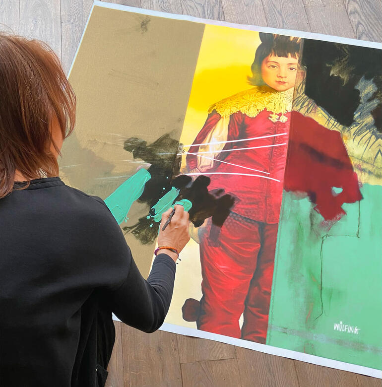 Anja Wülfing übermalt jedes Exemplar an einigen Stellen von Hand. Frau malt an einem Kunstwerk mit lebendigen Farben.
