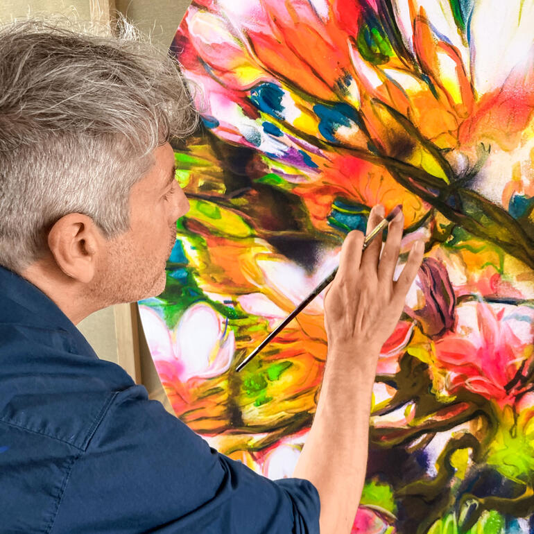 Mann malt mit Pinsel an blühendem Kunstwerk.