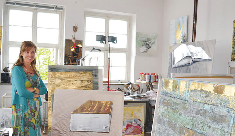 Beatrice Bues-Bohl Beatrice Bues-Bohl steht in ihrem Atelier vor mehreren Kunstwerken.