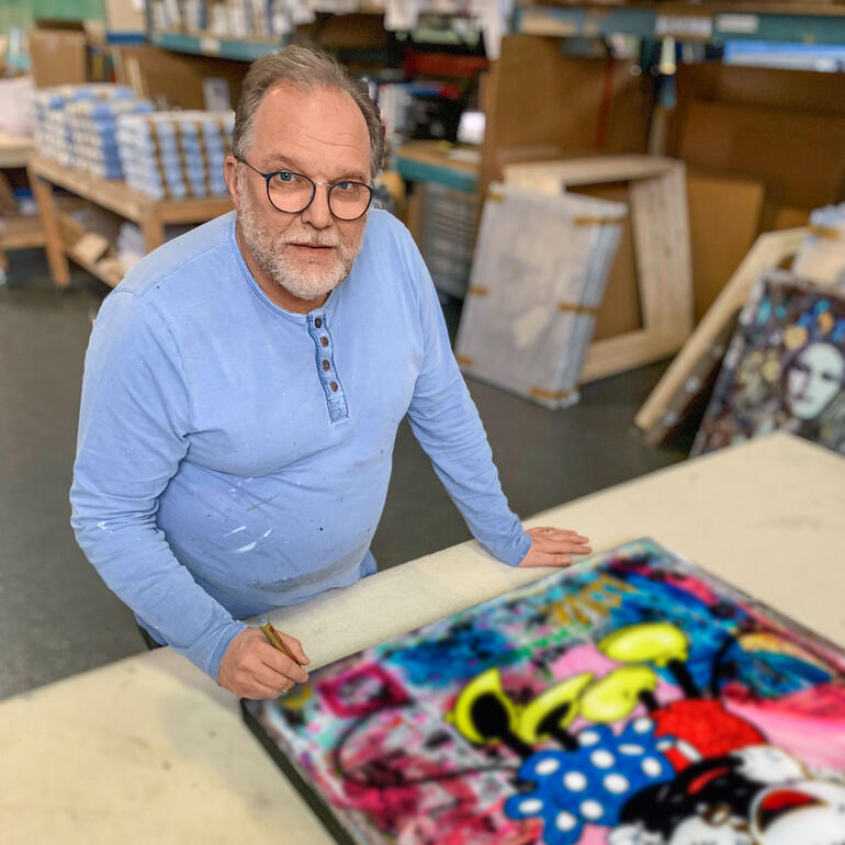 Devin Miles steht an einem Tisch und arbeitet an einem farbenfrohen Kunstwerk.