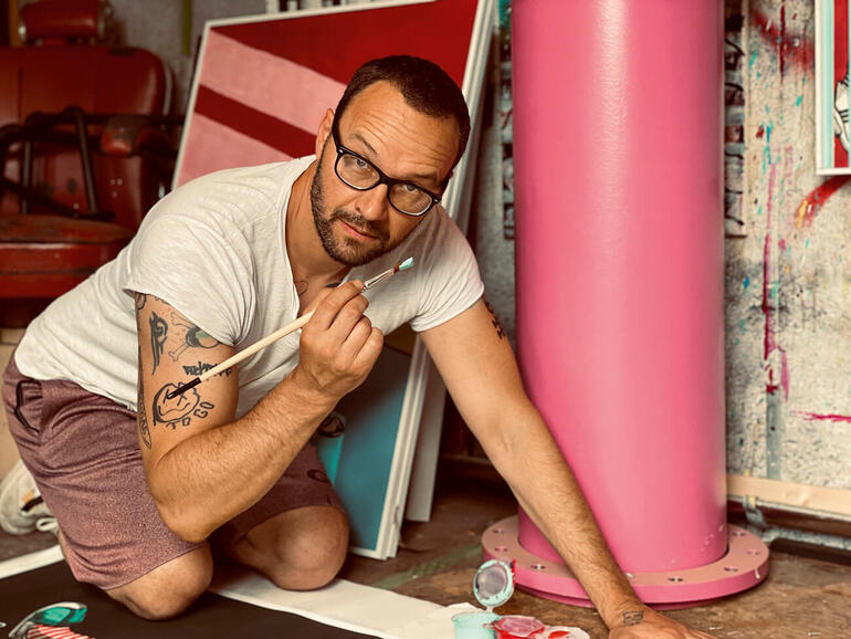 Ronny Kindt vom Künstler-Duo RON MILLER Ron Miller kniet und arbeitet an einem Kunstwerk mit einem Pinsel.