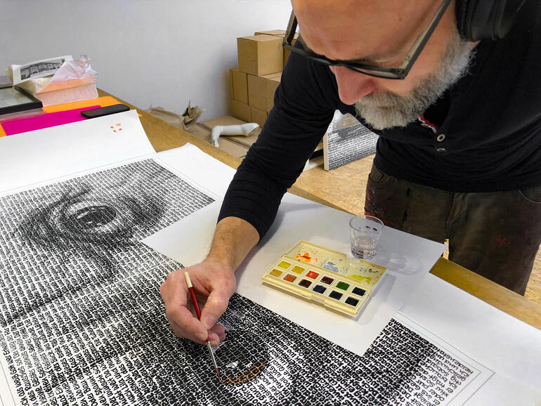 Ein Künstler malt mit Pinsel an einem großen Kunstwerk aus Text.