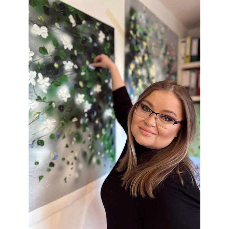 Anastassia Skopp malt an einer Wand mit weißen Blüten.