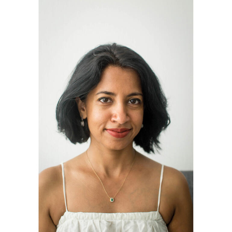 Rashmi Thodkar Rashmi Thodkar mit schwarzem Haar, tragt ein helles Top und lächelt gegen einen neutralen Hintergrund.